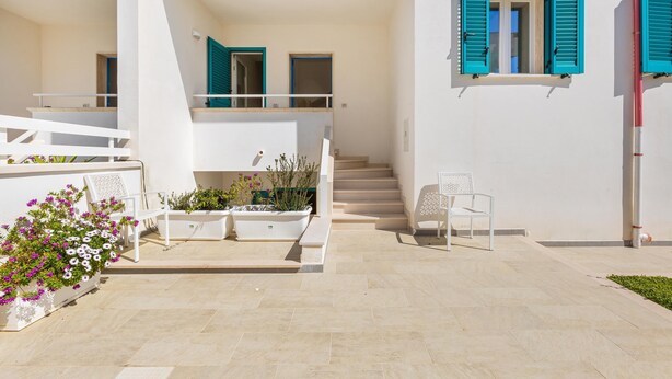 A modern building with a staircase leading to a balcony, white walls, and a window with blue shutters.