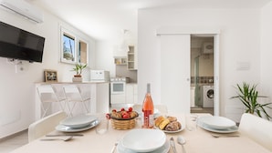 A modern kitchen with white cabinetry, a dining area with a table set for two, and a TV mounted on the wall.