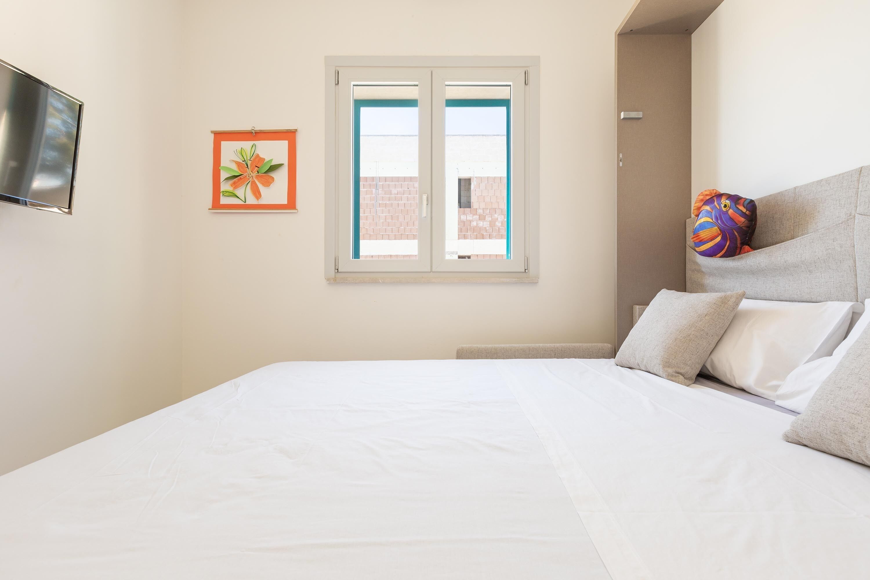 A bedroom with a bed, a window, a TV, and a colorful pillow.