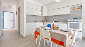 A modern kitchen with white cabinets, a dining table with orange accents, and a white oven.