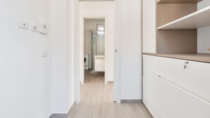 A narrow hallway with a light wooden floor, white walls, and a white cabinet with a beige countertop on the right.
