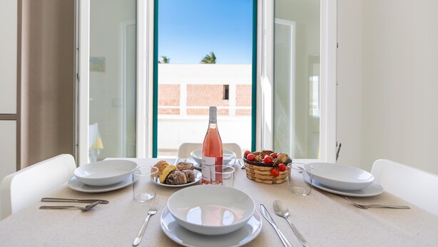 A dining table set with plates, glasses, cutlery, a bottle of wine, and a basket of fruit. - 3274 Residence Amida - Appartamento Sole by Barbarhouse (Maruggio)