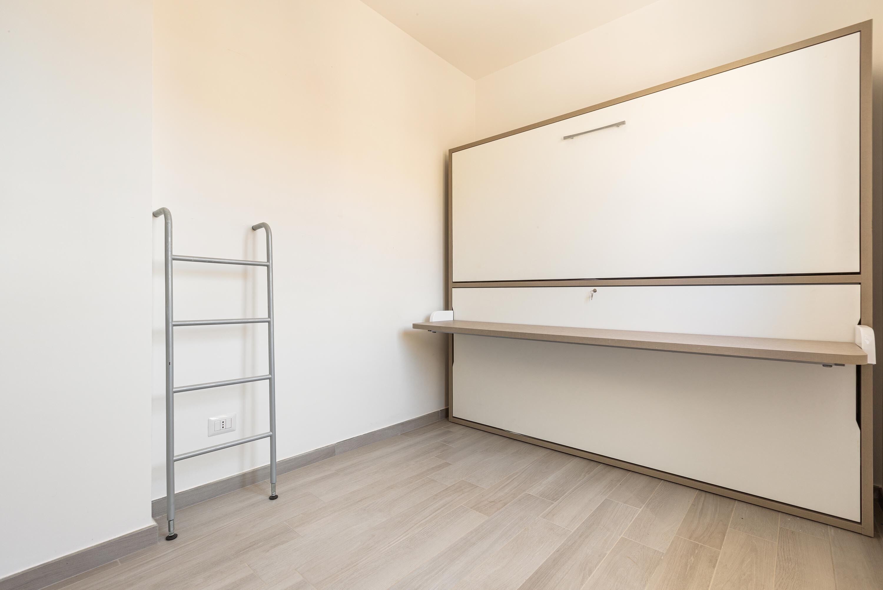 A room with a white wardrobe, a metal shelf unit, and a wooden floor.