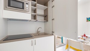 A compact kitchen with a built-in microwave, a sink, and a small dining area with a table and chairs. - 3274 Residence Amida - Appartamento Sole by Barbarhouse (Maruggio)