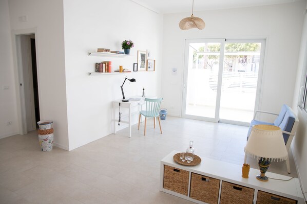 A bright, modern living room with a white sofa, a coffee table, and a lamp. There is a desk with a chair and a plant on the wall. - Villa Ravanica (Giannuzza) with pool 400m from the beach (Marina di Ragusa)