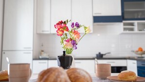 A kitchen with white cabinets, a black coffee maker, a vase with colorful flowers, and pastries on the counter. - Villa Ravanica (Giannuzza) with pool 400m from the beach (Marina di Ragusa)