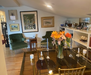 Uma sala de estar moderna com uma mesa de centro de vidro, poltronas verdes e um quadro grande na parede.