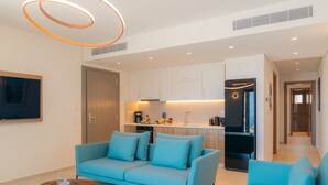 A modern living room with a blue sofa, a coffee table, and a kitchen area with cabinets and appliances. - Sigma Residences Boutique Hotel (Sifnos)