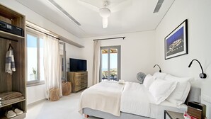 A modern bedroom with a bed, bedside table, TV, and a view of the outdoors. - Sigma Residences Boutique Hotel (Sifnos)