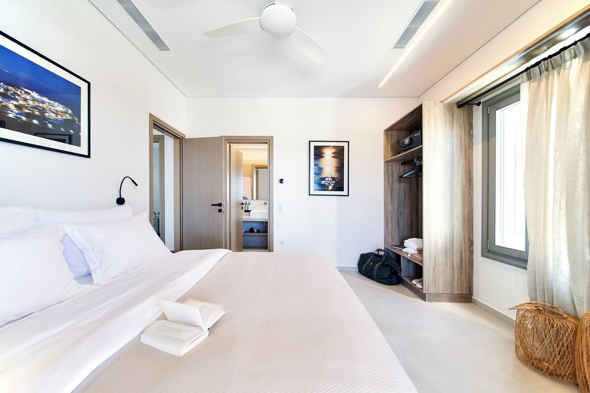 A modern hotel room with a large bed, a ceiling fan, a wardrobe, and a window with curtains.