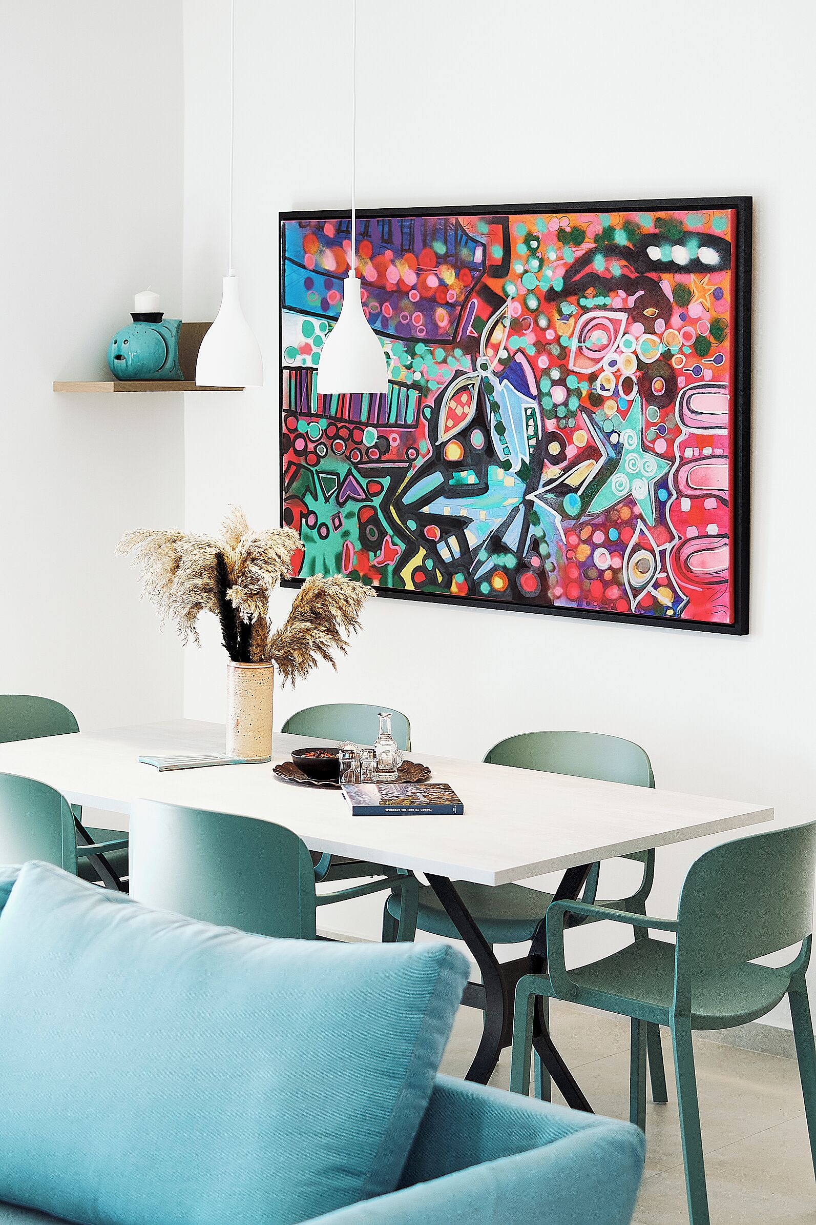 A dining area with a white table, teal chairs, and a colorful abstract painting on the wall.