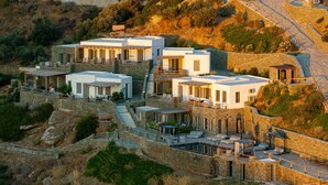 A hillside property with multiple white buildings, stone walls, and outdoor seating areas. - Sigma Residences Boutique Hotel (Sifnos)