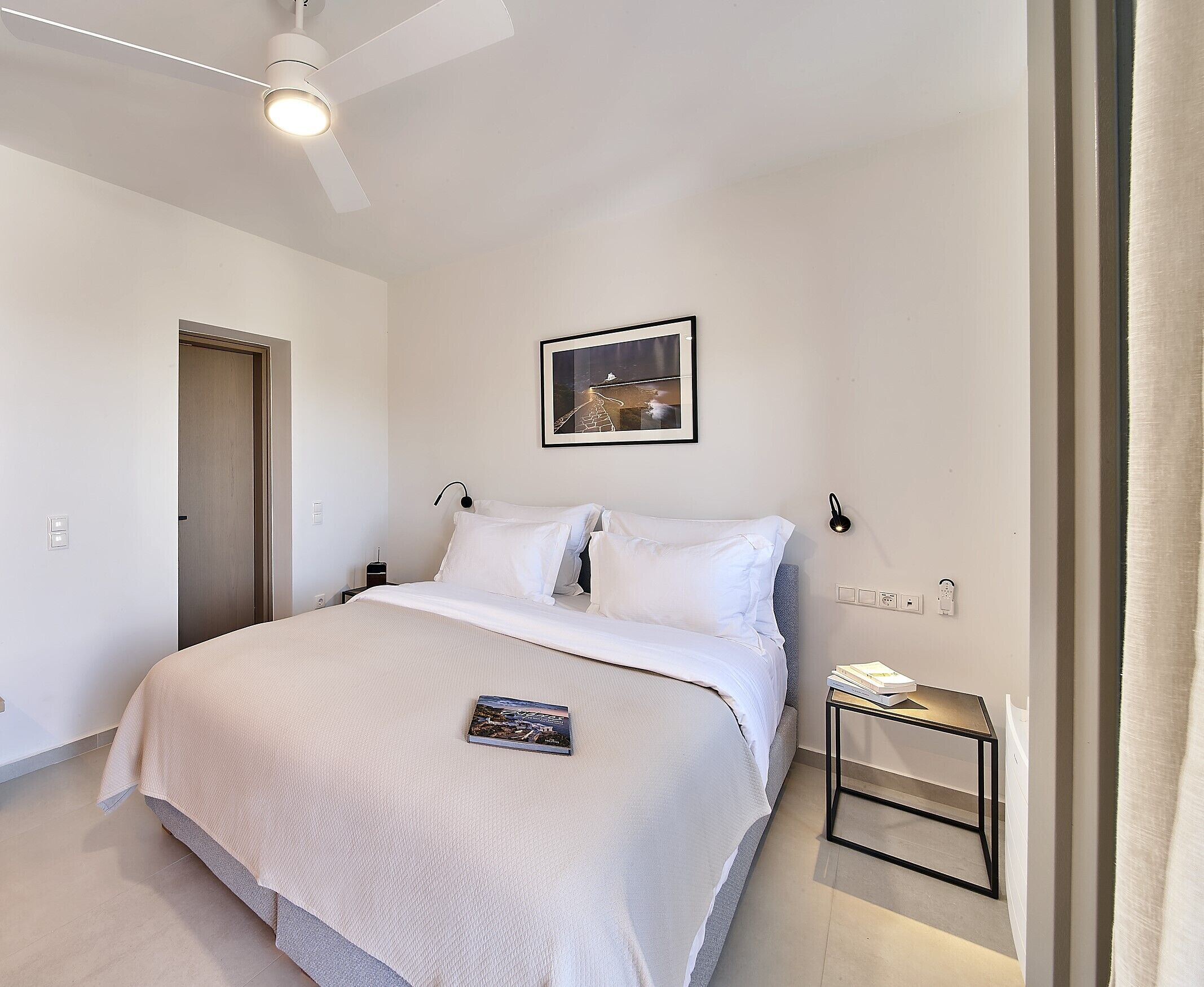Een keurig opgemaakt slaapkamer met een bed, nachtkastje, wandlamp en plafondventilator.