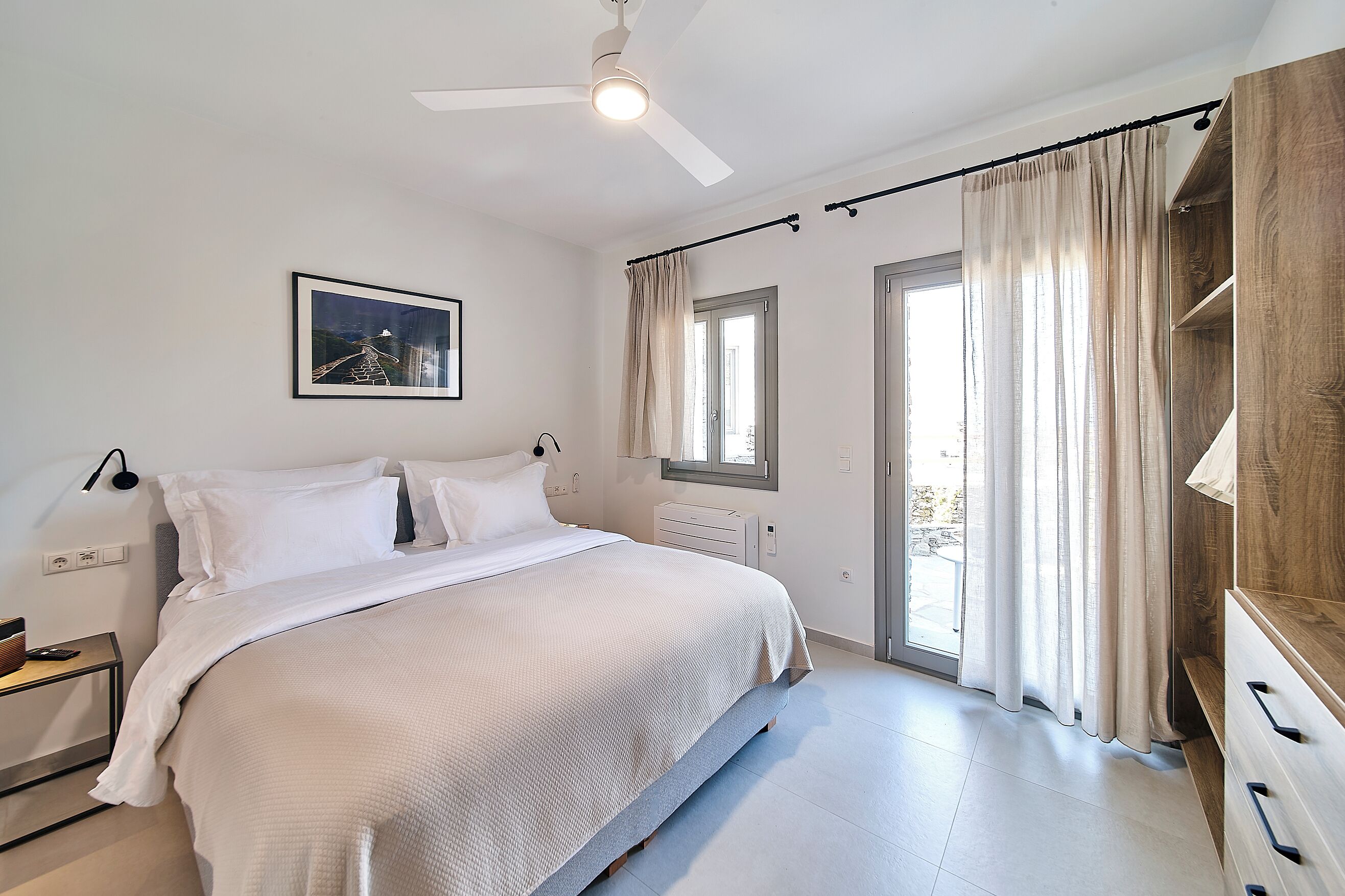A bedroom with a bed, bedside table, lamp, window, and curtains.