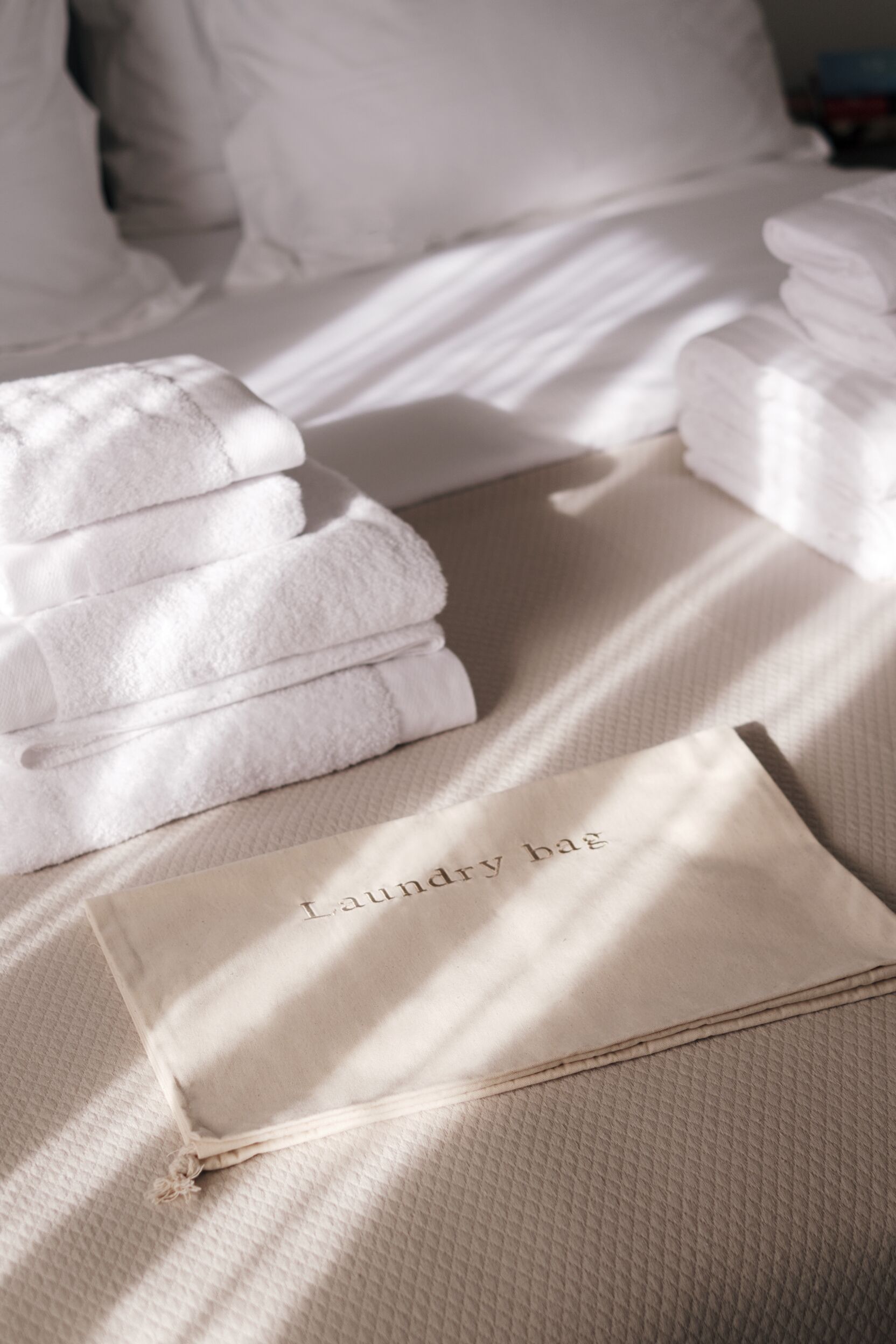 A neatly made bed with folded white towels and a beige laundry bag on it.