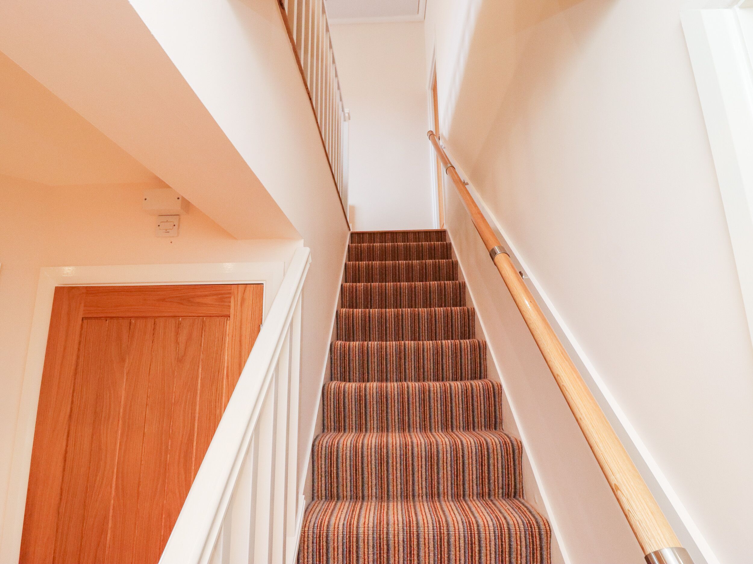 A staircase with wooden handrails and striped carpeted steps.