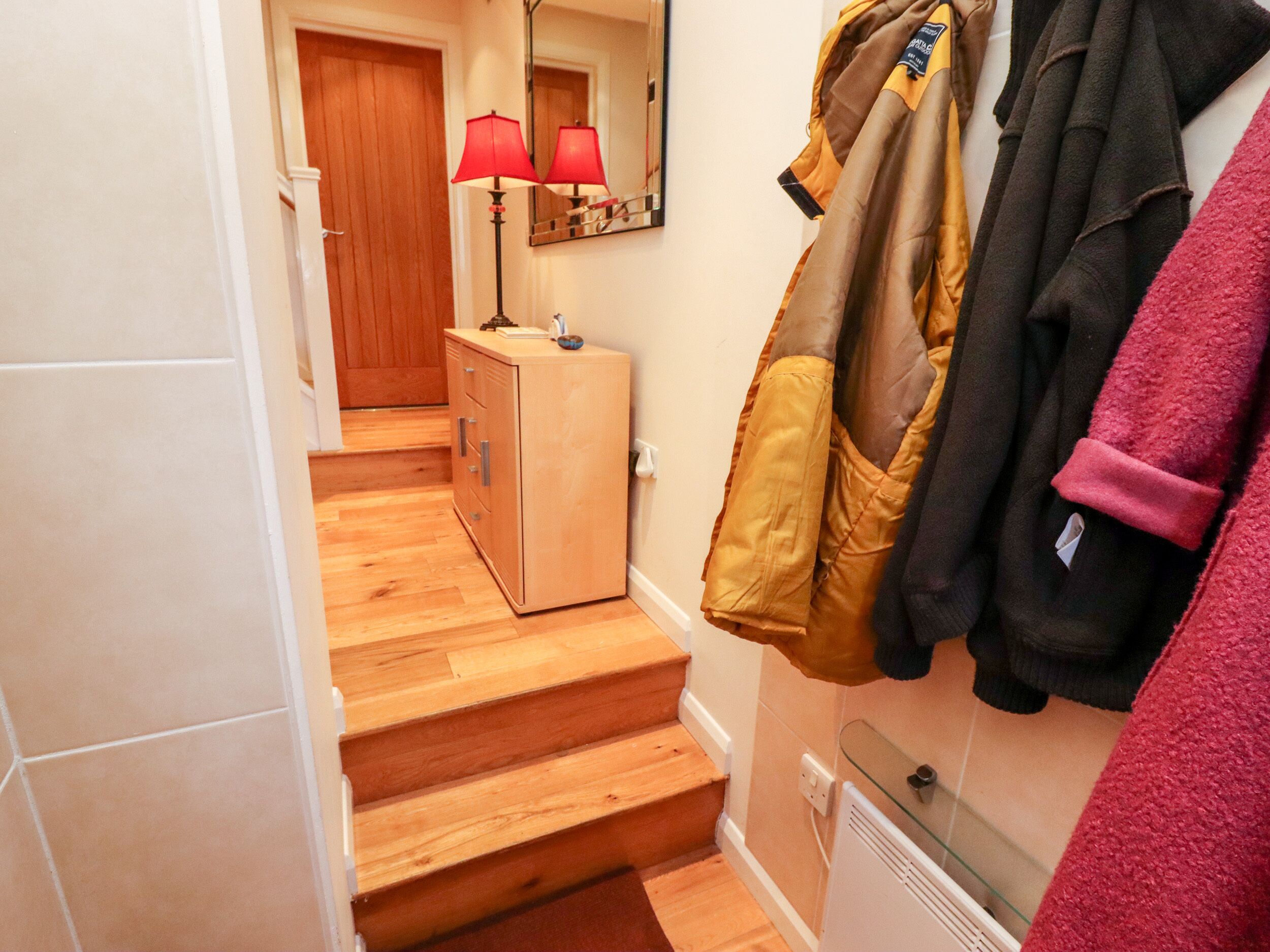 A hallway with wooden stairs, a wooden cabinet, a mirror, and a radiator.