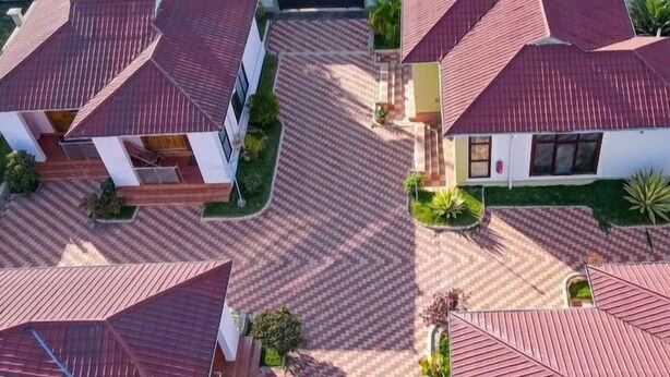 A residential area with multiple houses featuring red-tiled roofs and a central courtyard with patterned paving. - samanene hotels limited (Mwanza)