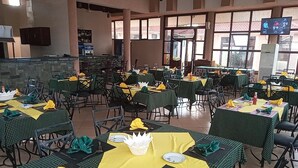 A spacious dining area with multiple tables set for dining, featuring green checkered tablecloths and yellow napkins. - samanene hotels limited (Mwanza)