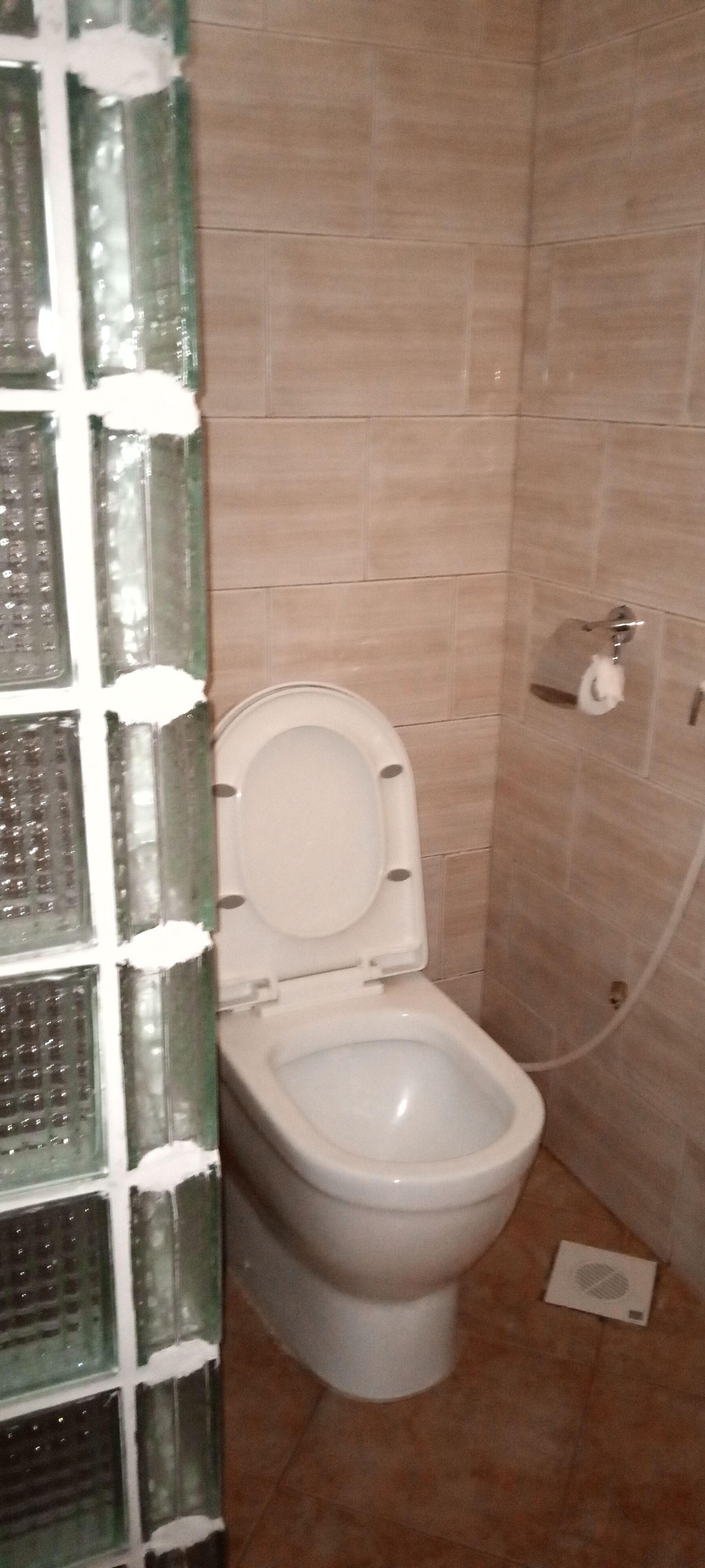 Un baño con inodoro, paredes de azulejos y zona de ducha.