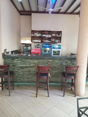 A bar area with a stone counter, two wooden chairs, and shelves stocked with various liquor bottles.