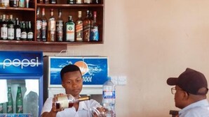 A bar area with a counter, a Pepsi refrigerator, and a water dispenser. There are wooden chairs and a stone wall in the background. - samanene hotels limited (Mwanza)