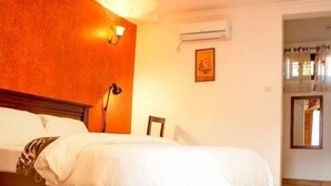 A hotel room with a large bed, a nightstand, a lamp, an air conditioning unit, and a framed picture on the wall. - samanene hotels limited (Mwanza)