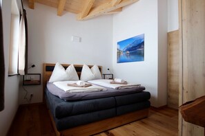 Une chambre à coucher avec un lit en bois, une tête de lit ornée de trois oreillers blancs, un matelas bleu foncé et une serviette roulée posée sur le lit.