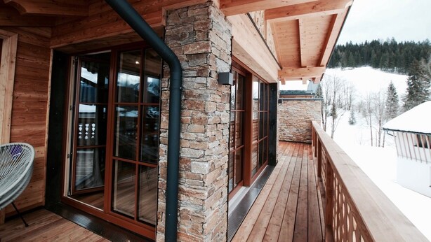 Una cabaña de madera con fachada de piedra, puertas correderas de vidrio grandes y una terraza de madera con vista a un paisaje nevado.