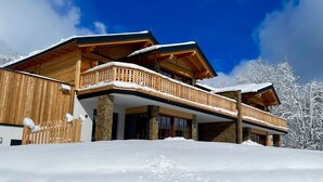 Un edificio de estilo chalet con fachada de madera, cimientos de piedra y un balcón con tejado cubierto de nieve.