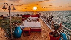 Une terrasse avec des chaises longues et une vue sur le coucher de soleil sur la mer.