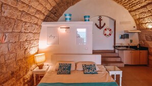 Une pièce chaleureuse avec un mur en pierre, un lit recouvert d’une courtepointe turquoise et une petite kitchenette.