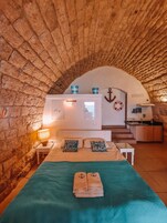 Una habitación acogedora con pared de piedra, cama con colcha color turquesa y una pequeña kitchenette.