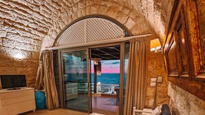 Une pièce chaleureuse avec un plafond en pierre, un canapé, une table et une vue sur la mer par une porte vitrée.