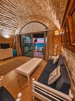 Una habitación acogedora con techo de piedra, un sofá, una mesa y vistas al mar a través de un ventanal.