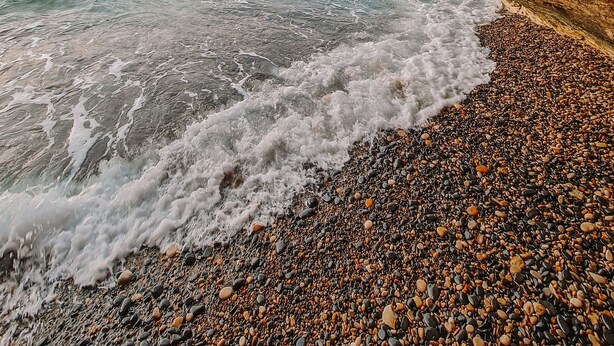 Une grotte rocheuse qui s’ouvre sur une plage de galets, où les vagues viennent se briser.