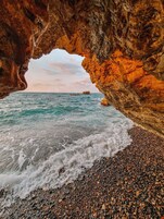 Una cueva rocosa que se abre a una playa de piedras y olas.