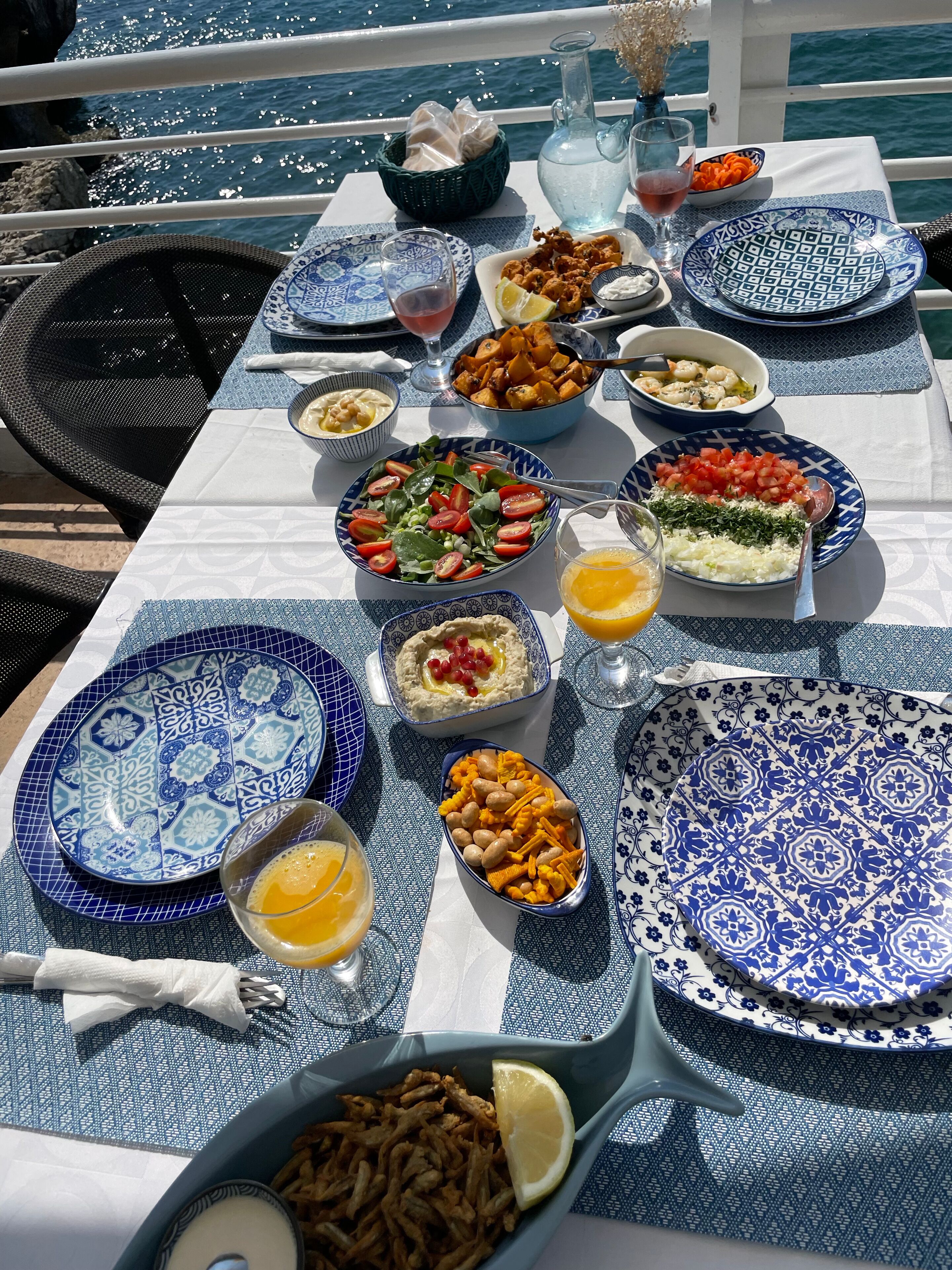 A table set with various dishes, including salads, dips, and snacks, on a boat deck with a view of the sea.