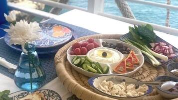 A table with a variety of food items including flatbreads, hummus, olives, and vegetables, set against a scenic ocean view.