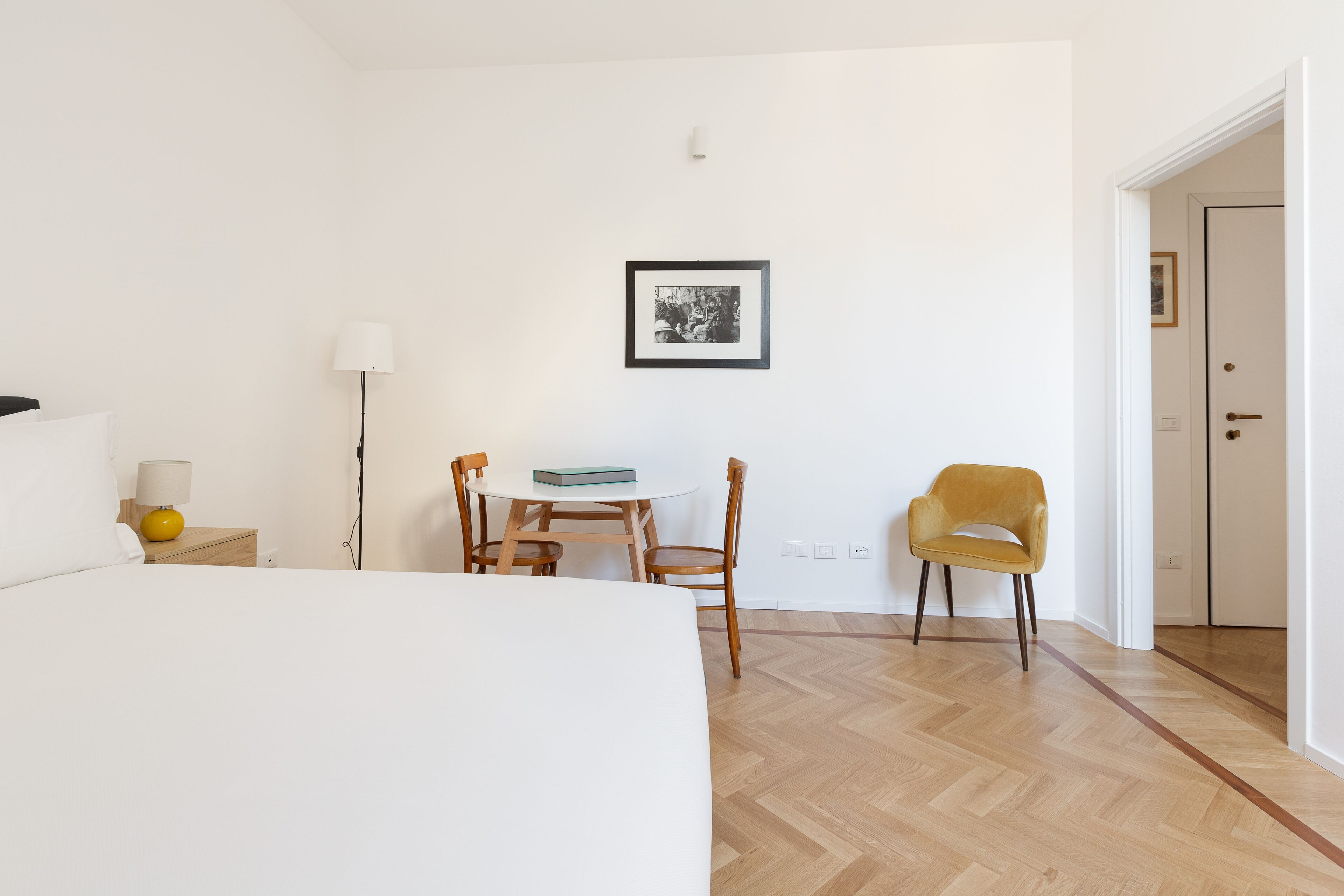 Ett hotellrum med en säng, ett skrivbord med en stol, en lampa och en inramad tavla på väggen.