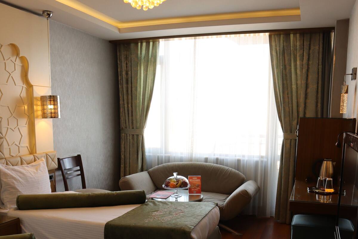 Una habitación de hotel con una cama, dos sofás, un escritorio y un ventanal con cortinas.
