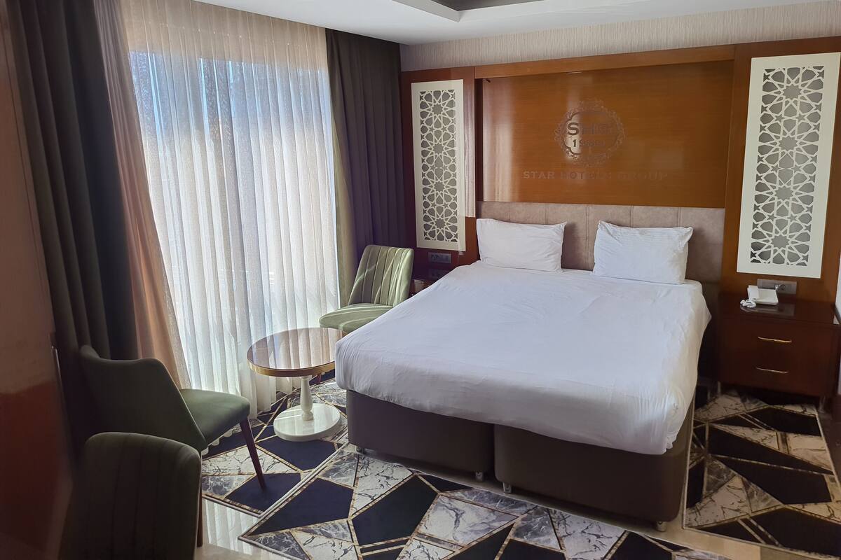 Una habitación de hotel con una cama grande, una silla, una mesita pequeña y un cabecero decorativo.