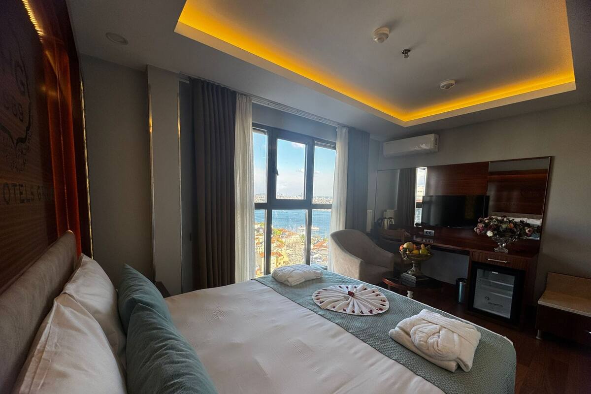 Habitación de hotel con una cama grande, un escritorio con televisor, vista a la ciudad y balcón.