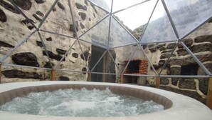 Un jacuzzi en una habitación con paredes de piedra y techo de vidrio geométrico.