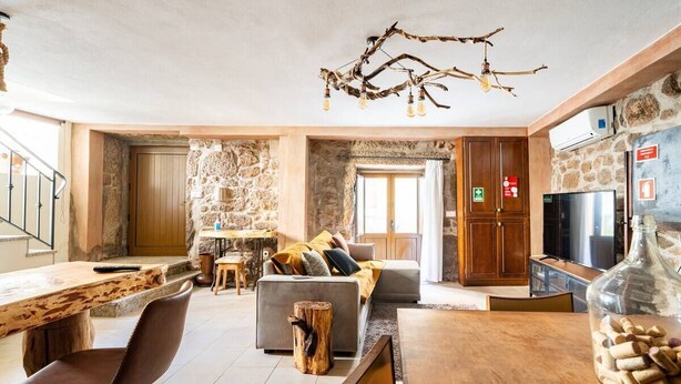 Un espacio acogedor con pared de piedra, una mesa de madera para comer, un sofá y una televisión.