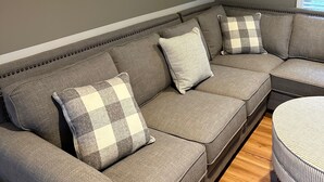 Um sofá modular com almofadas xadrez, um quadro pendurado na parede e uma janela com persianas.