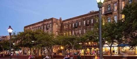 A public square with benches and trees, surrounded by historic buildings with multiple stories and windows.