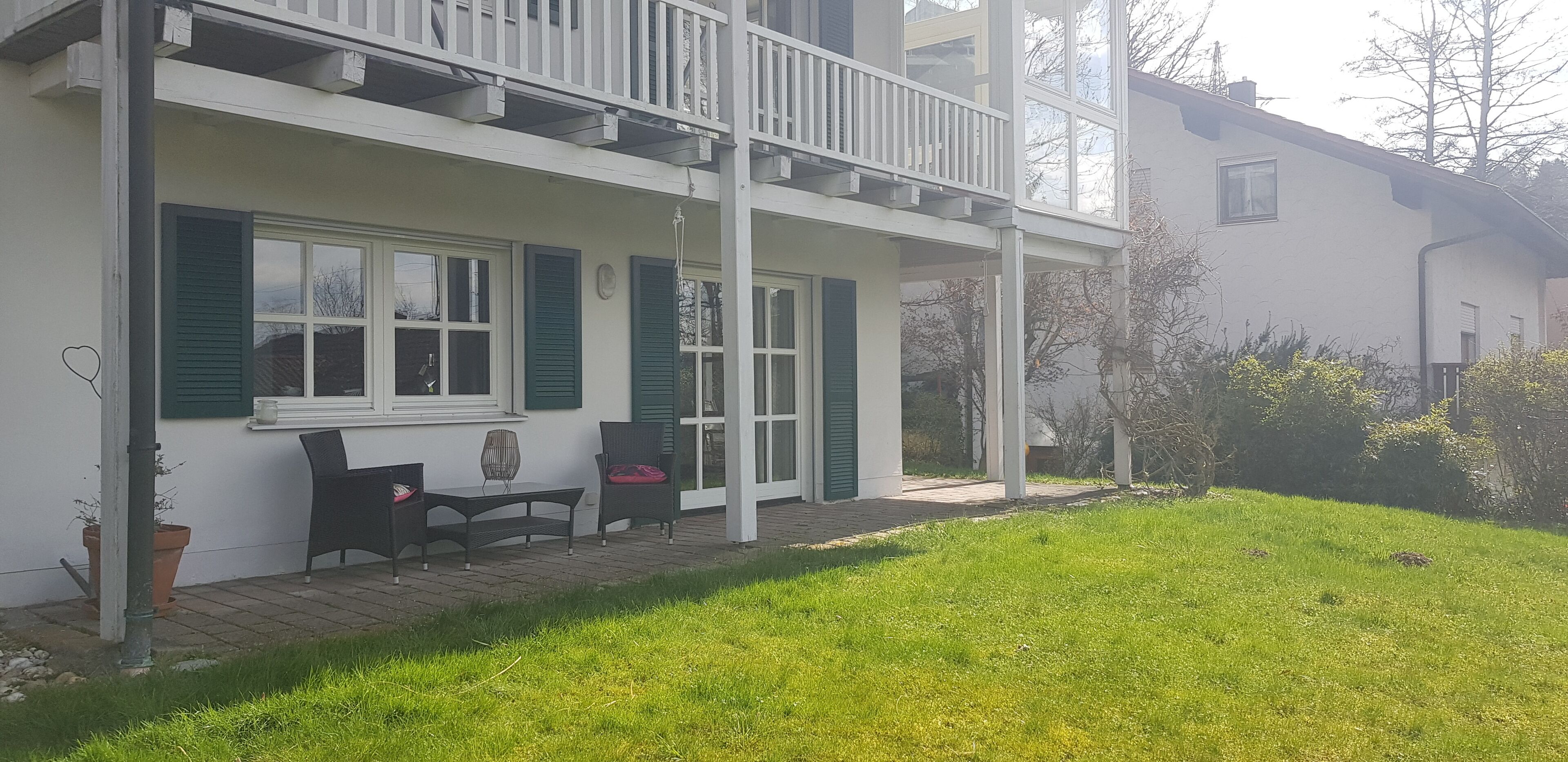 A two-story house with a balcony, a small patio with a table and chairs, and a well-maintained lawn.
