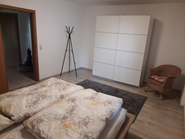 A bedroom with a bed, a wardrobe, a chair, and a floor lamp.