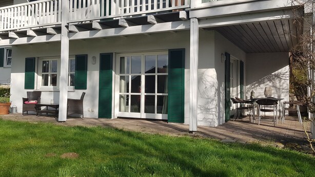 Un bâtiment blanc avec des volets verts, une véranda et du mobilier d’extérieur.